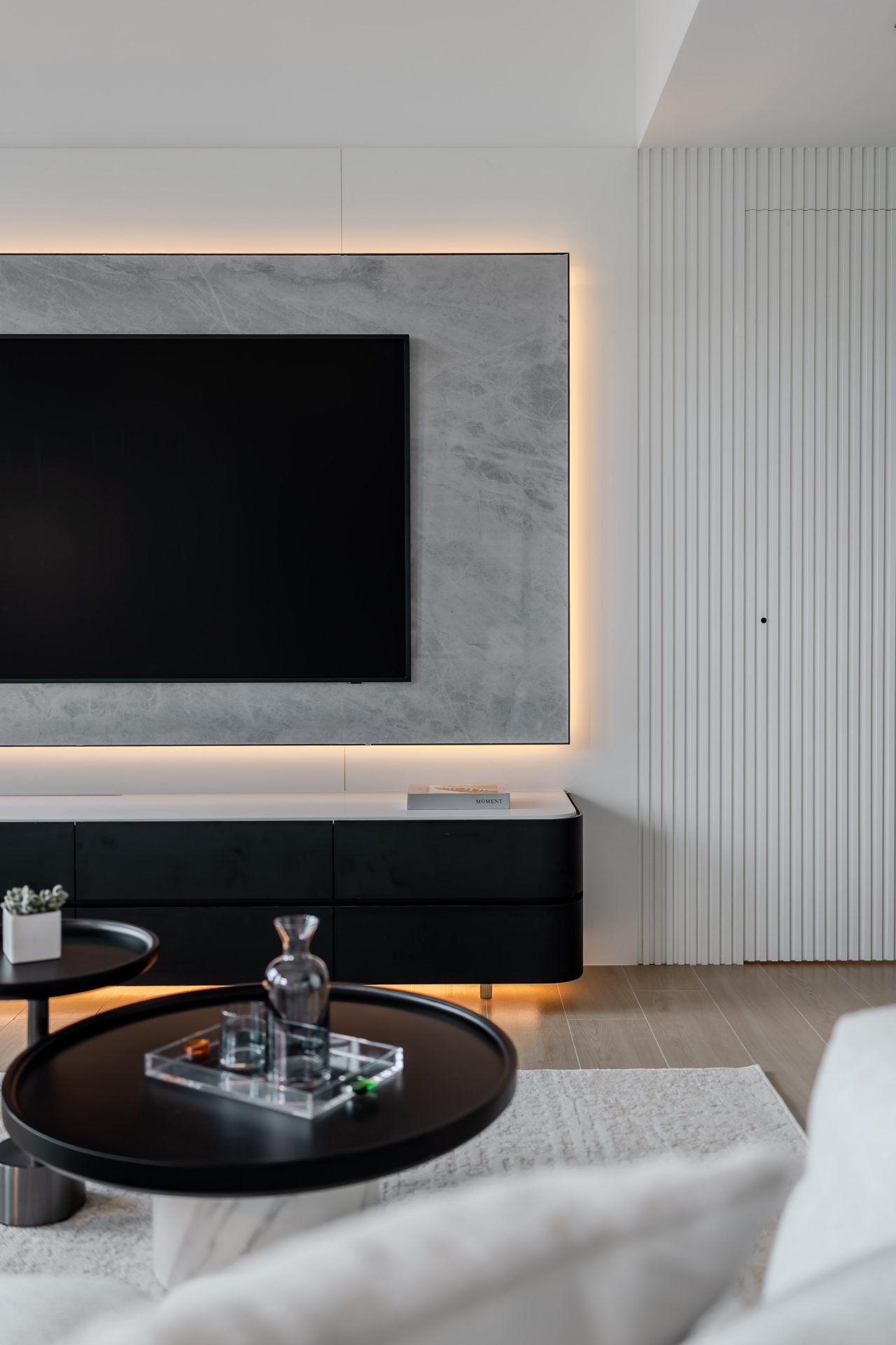 Double Cove — stone TV wall with a dark low cabinet and white fluted wall detail