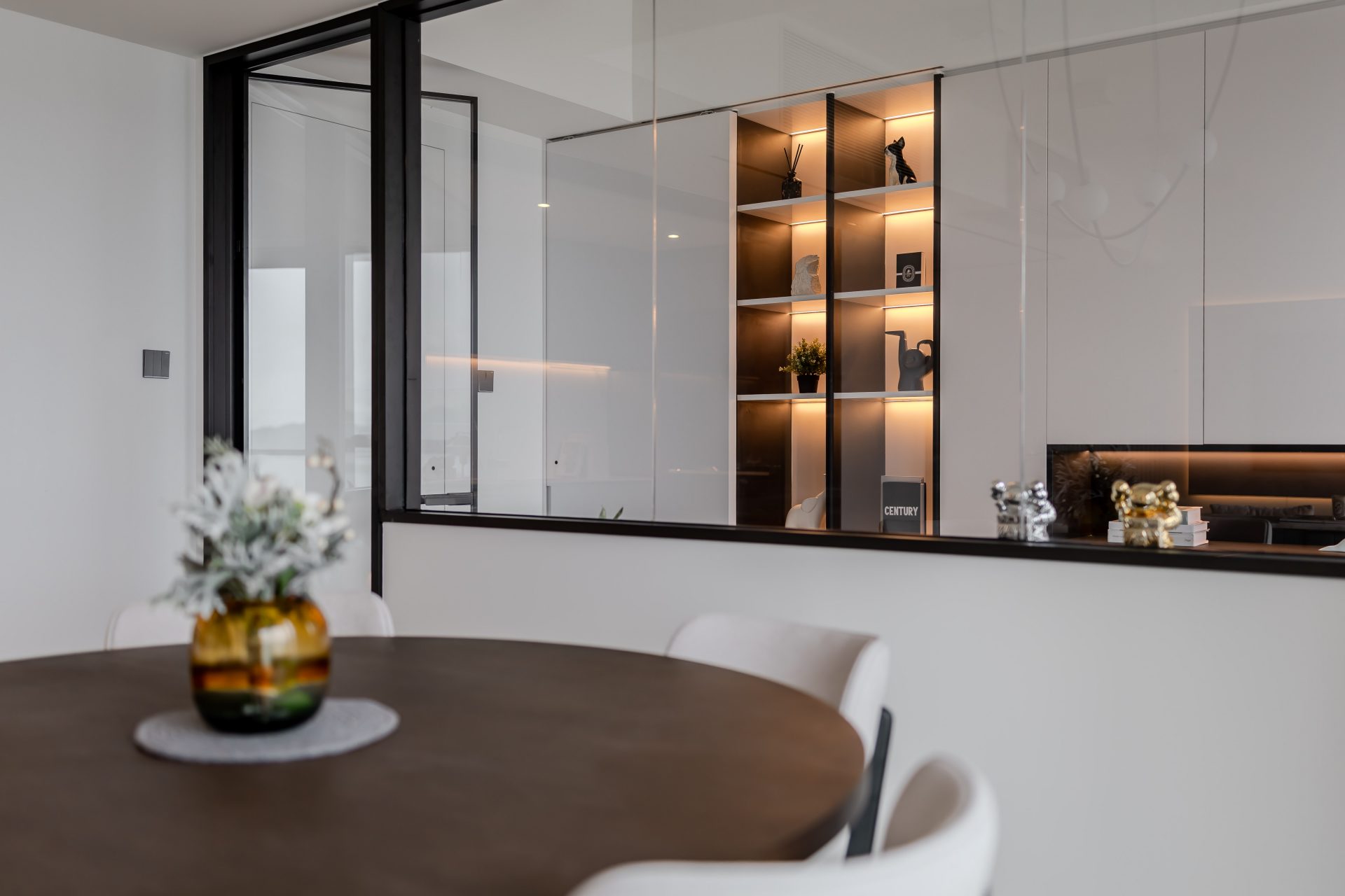 Double Cove — round dining table facing the grey-green kitchen and illuminated display cabinet