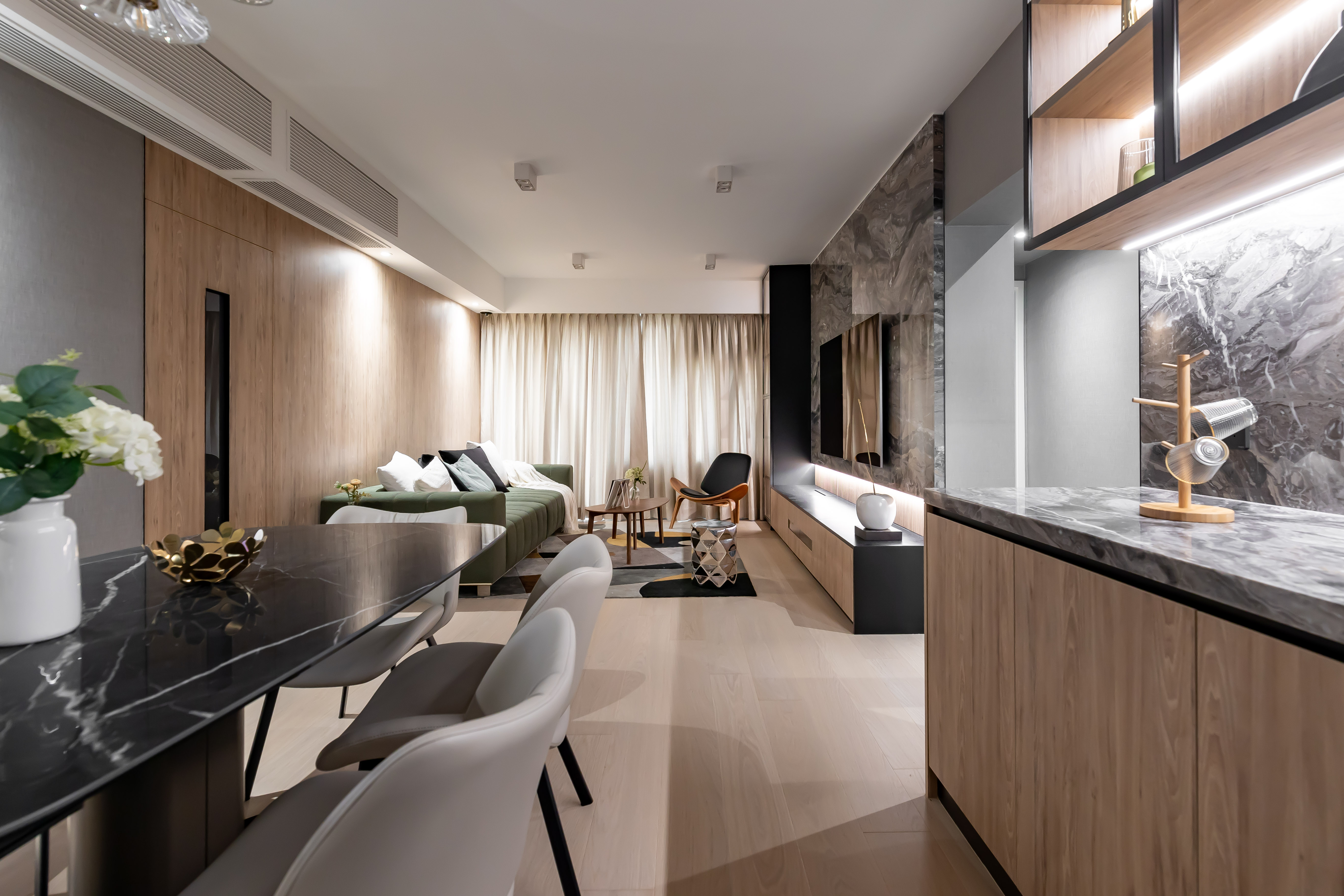 Living and dining room featuring a black marble dining table, green sofa, marble TV wall, wood paneling, and light wood flooring.