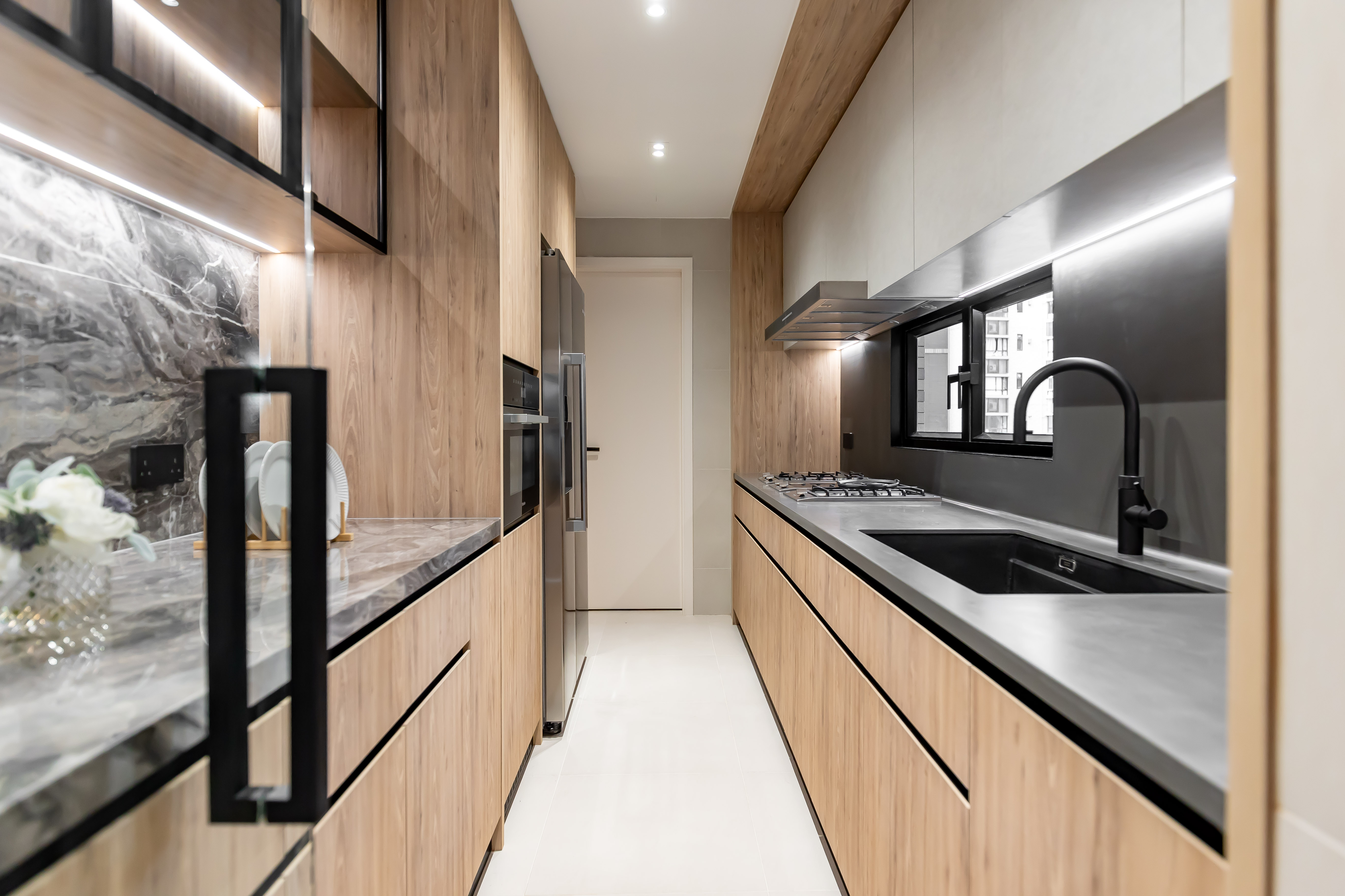 A modern kitchen featuring wood-grain cabinets, a grey countertop, a black sink, and built-in stainless steel appliances.