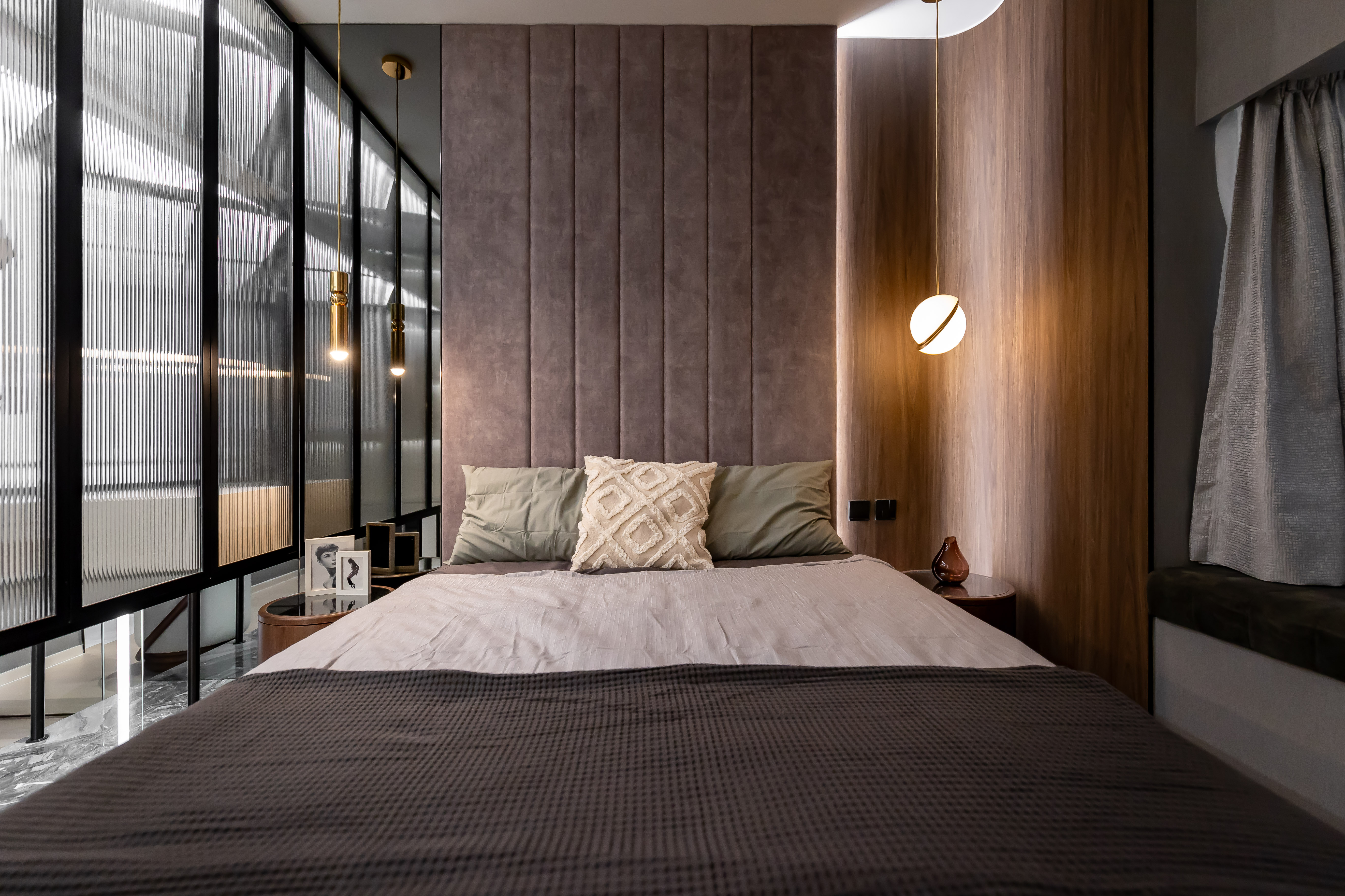 A modern bedroom featuring a bed with a padded headboard, wood paneling, and a glass partition with black frames.