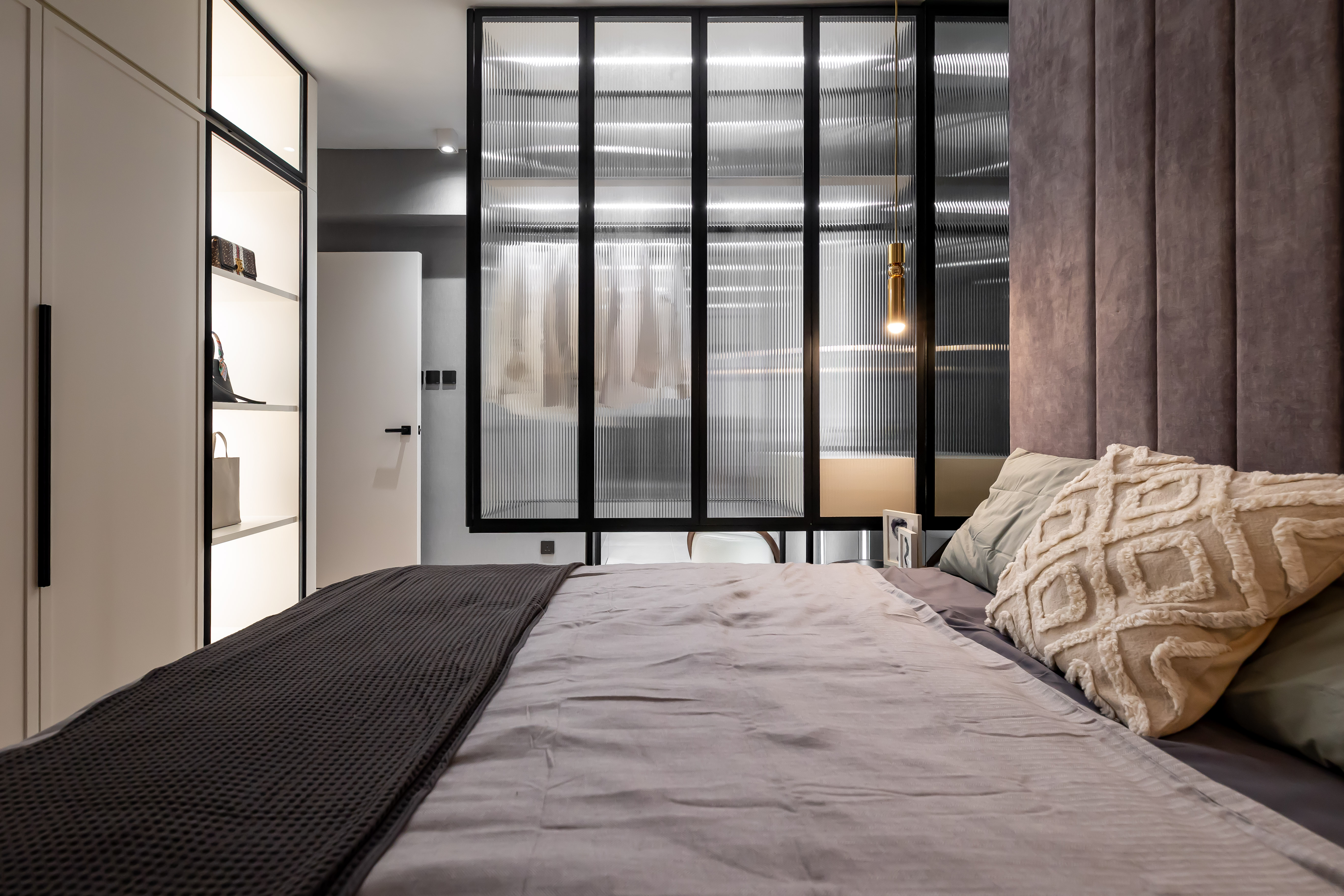 A modern bedroom featuring a bed with grey bedding, a glass-enclosed wardrobe, and an illuminated display cabinet.
