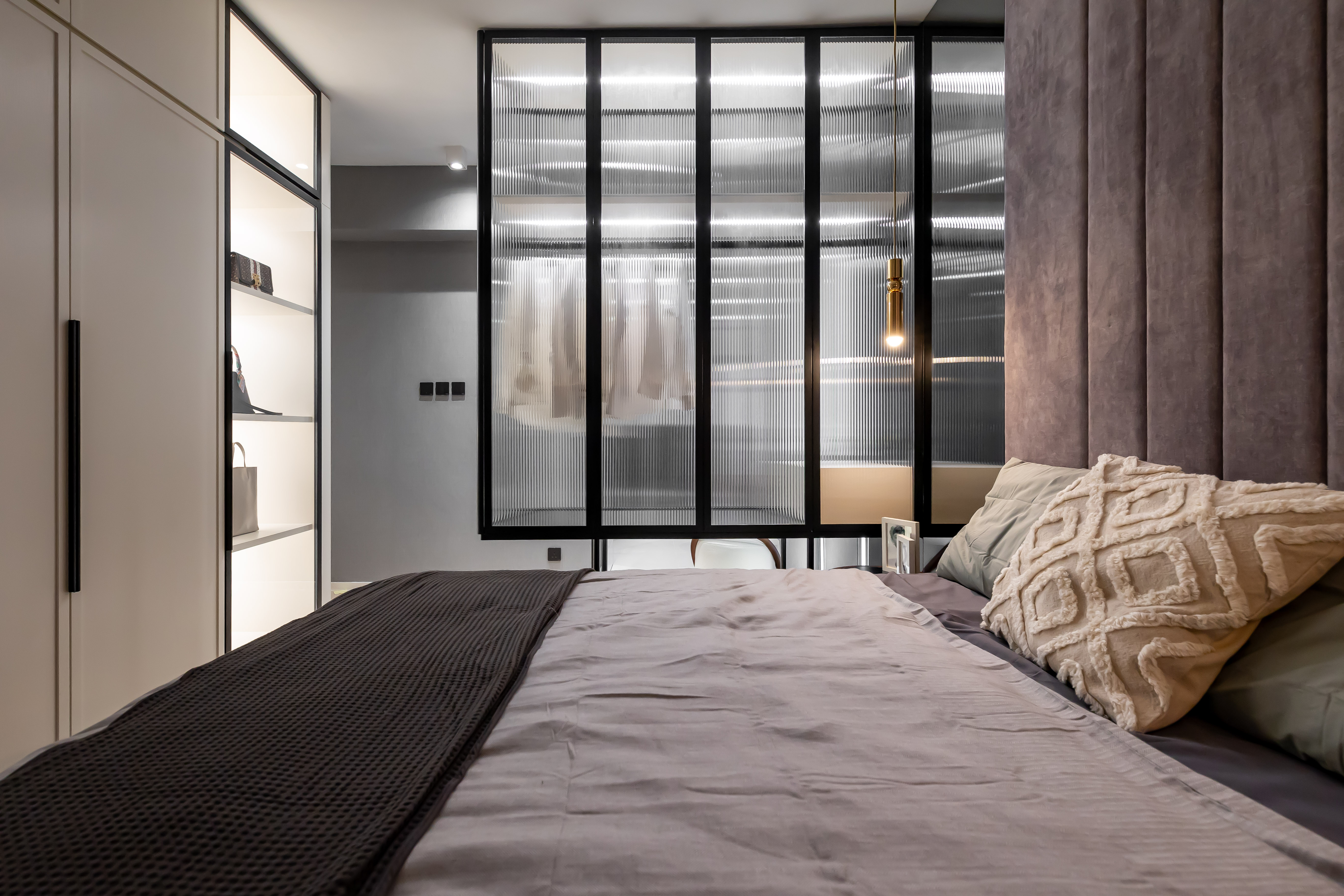 Modern bedroom featuring a double bed, purple upholstered headboard, fluted glass partition with black frames, and a white wardrobe.