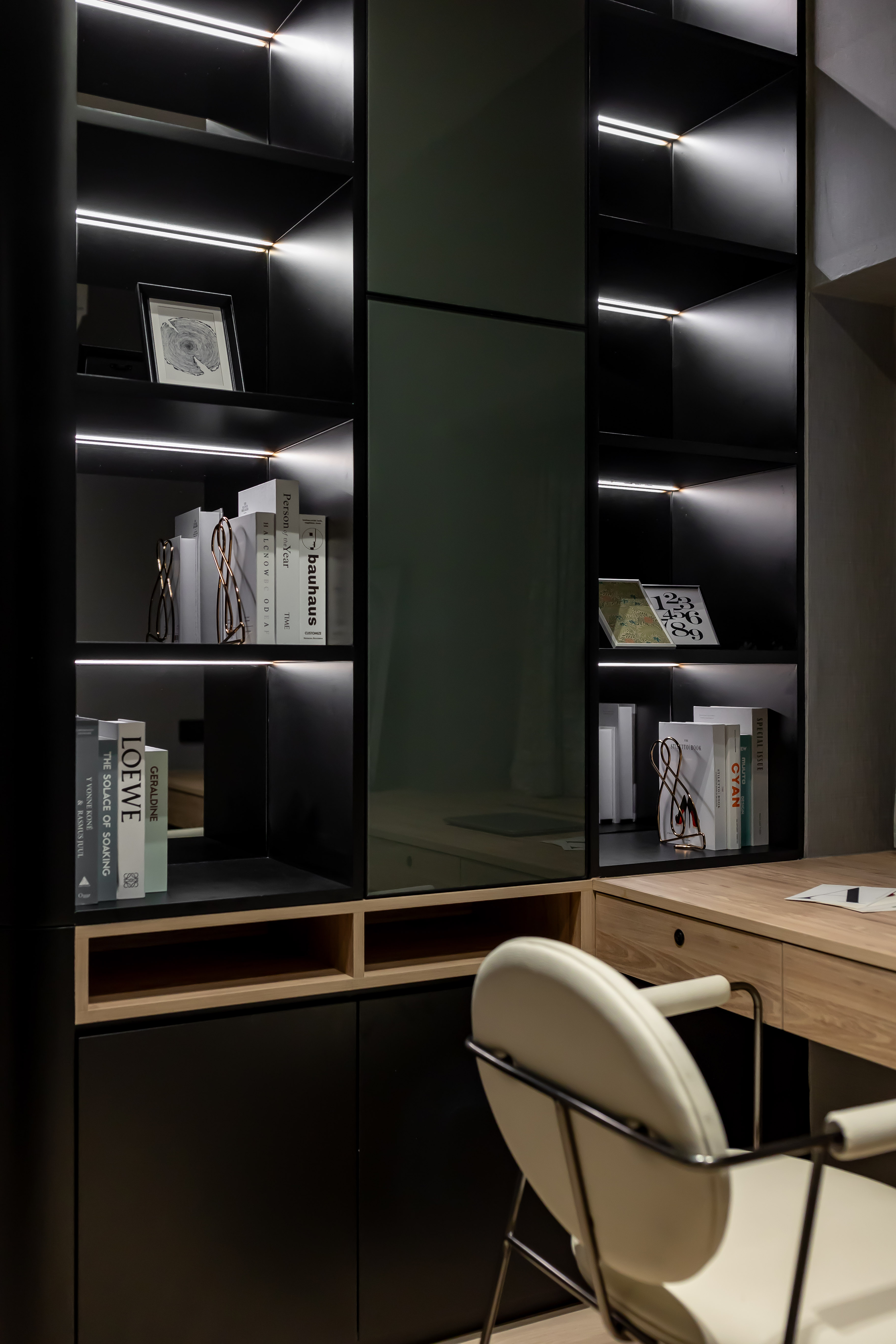 A study room featuring a black built-in bookshelf with LED lighting, a wooden desk, and a white chair.