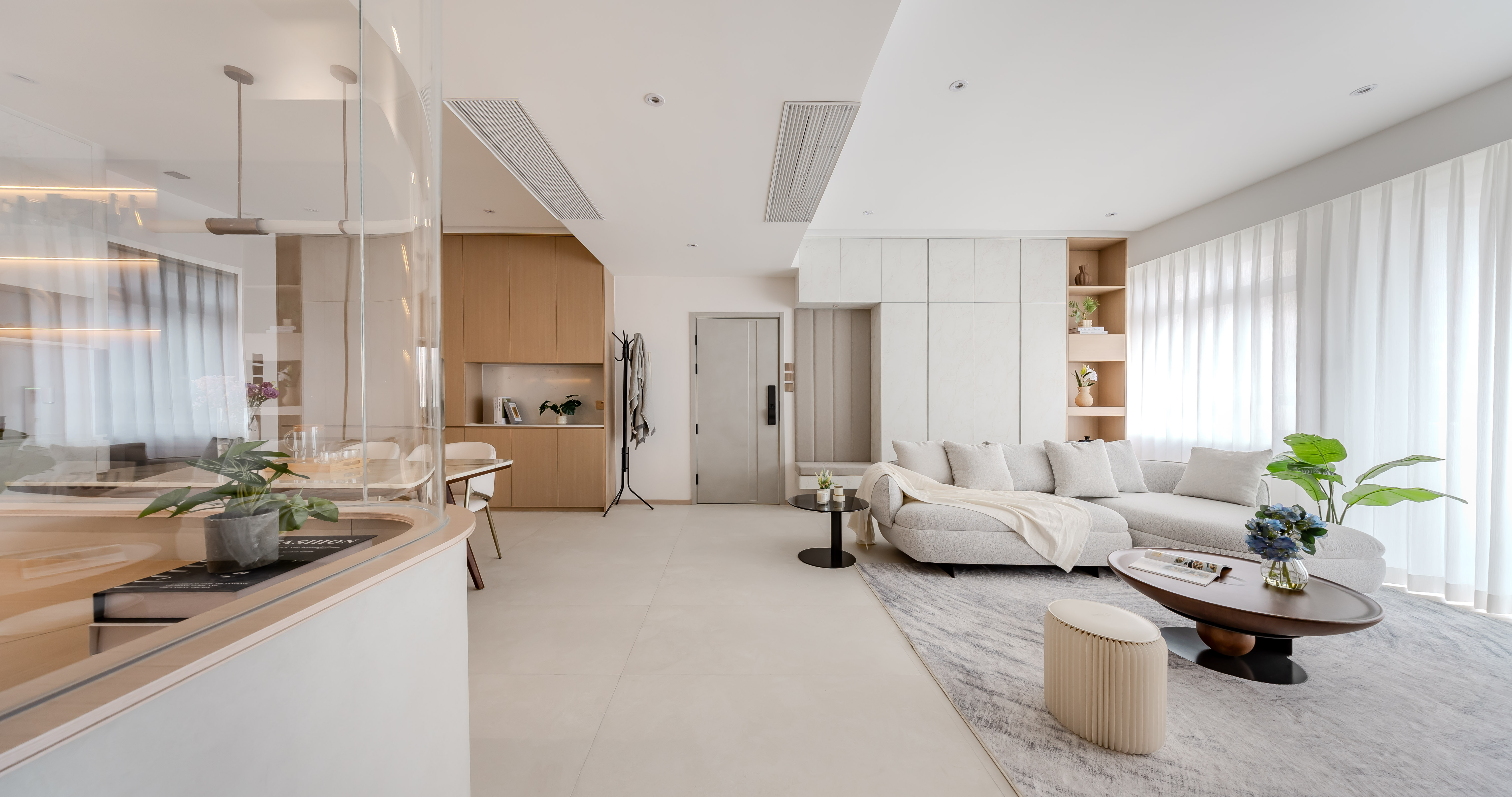 Bright living room with a light L-shaped sofa, dark oval coffee table, white built-in cabinets, and a glass partition.