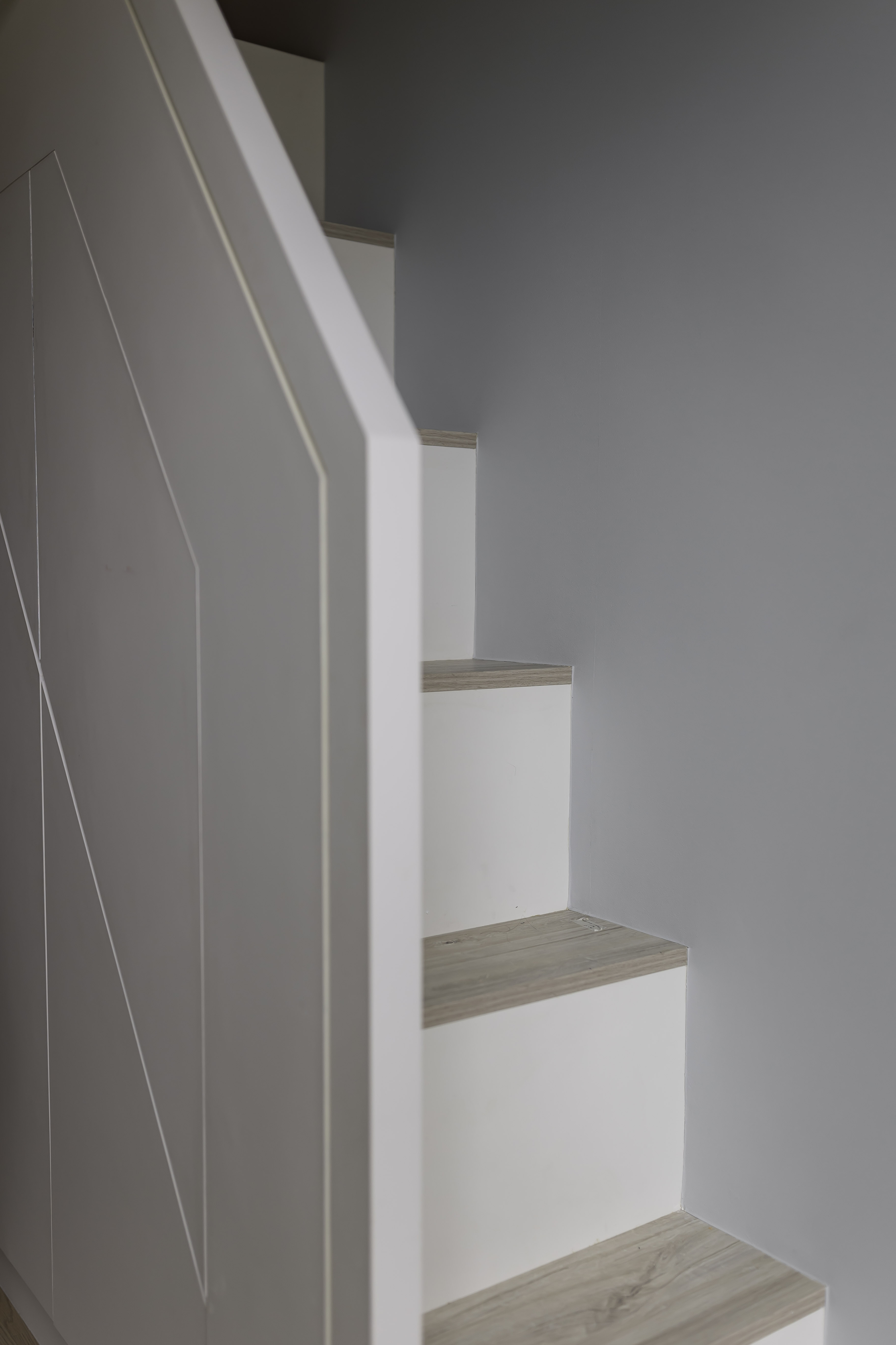 A wooden staircase with white risers and a white side panel featuring geometric lines next to a grey wall.