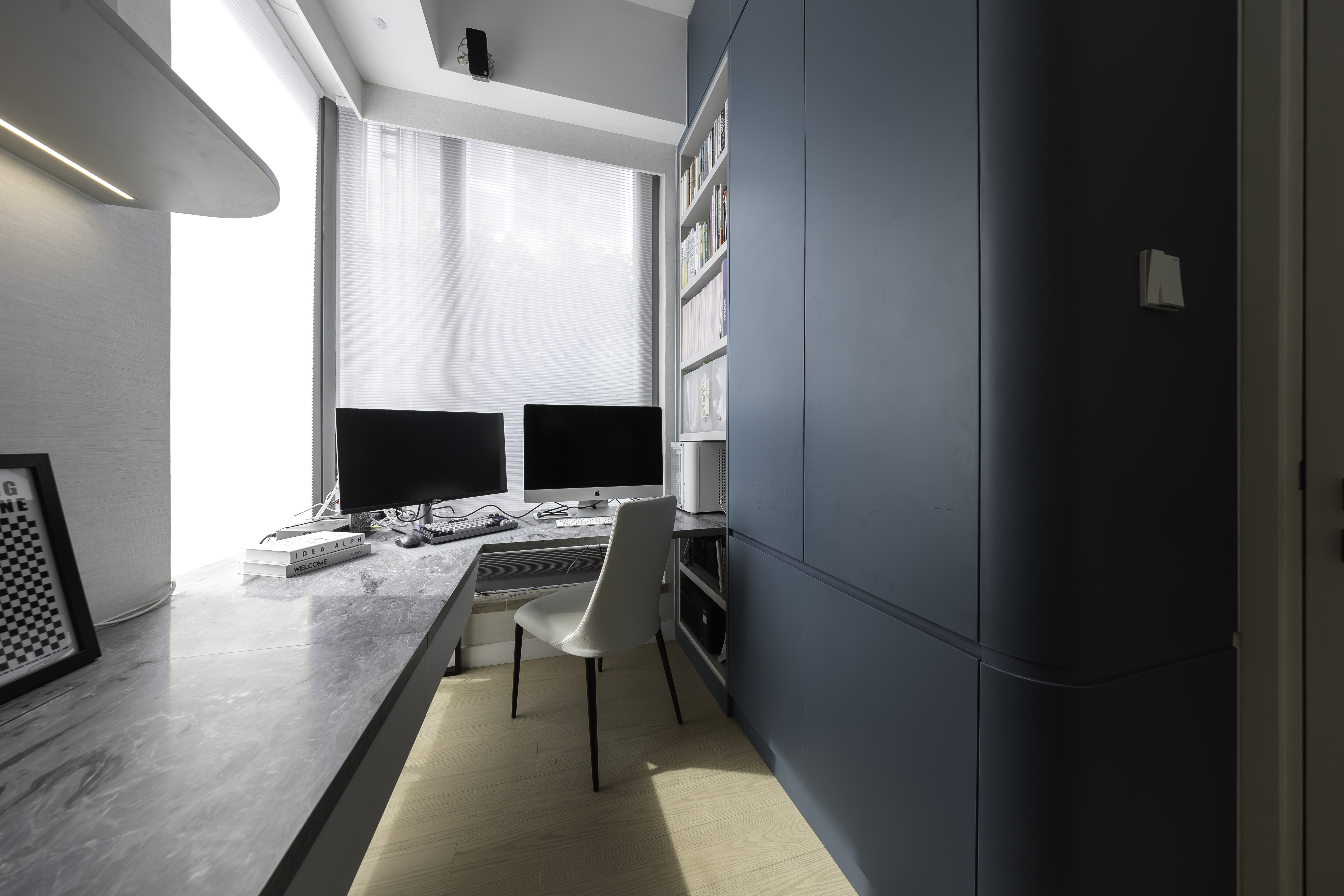 A modern study room featuring a grey marble desk, two monitors, a white chair, and a large teal storage cabinet.