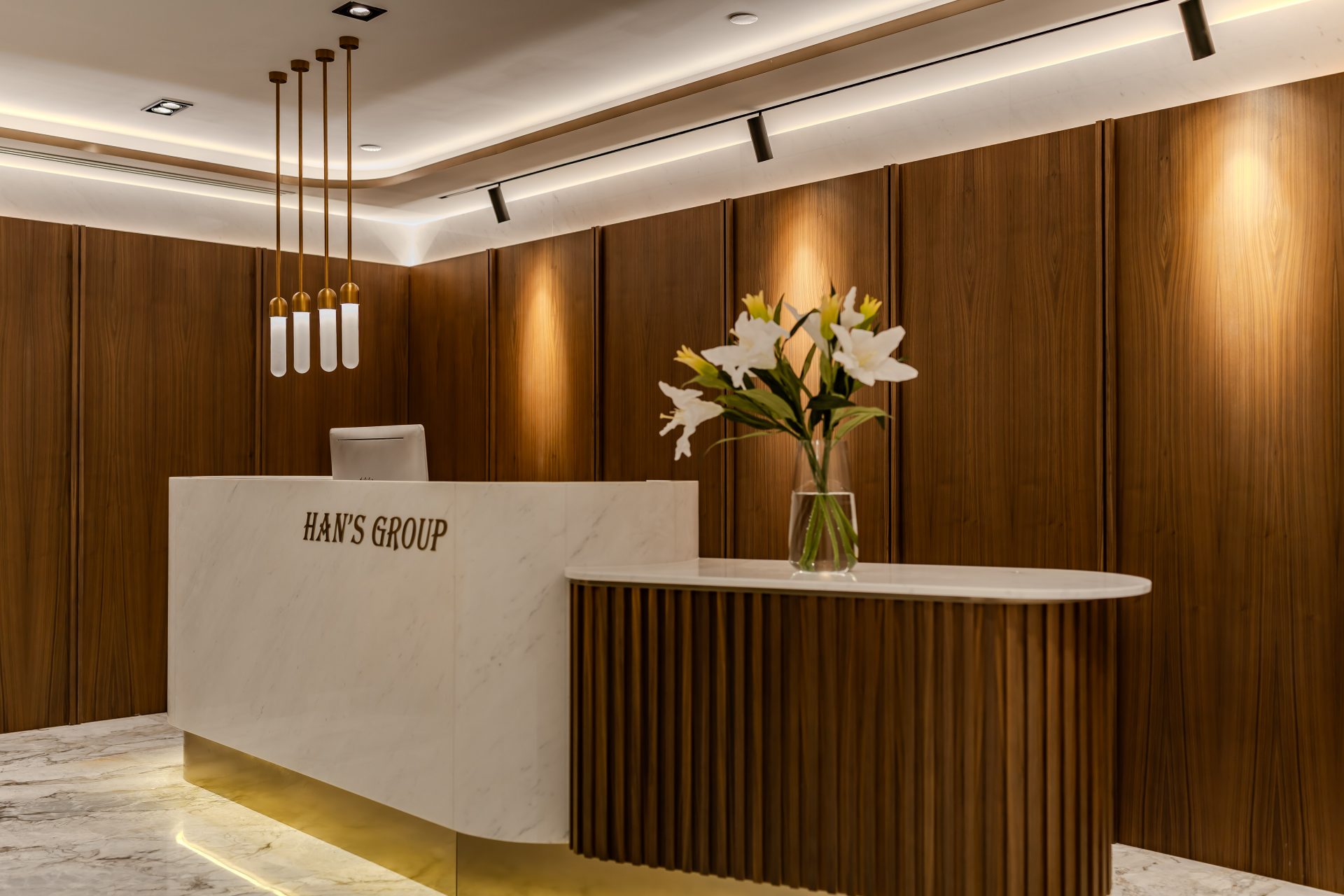 Han’s Laser Office — The reception area combines marble and timber slats with a feature pendant light, establishing an elegant and welcoming first impression for visitors.