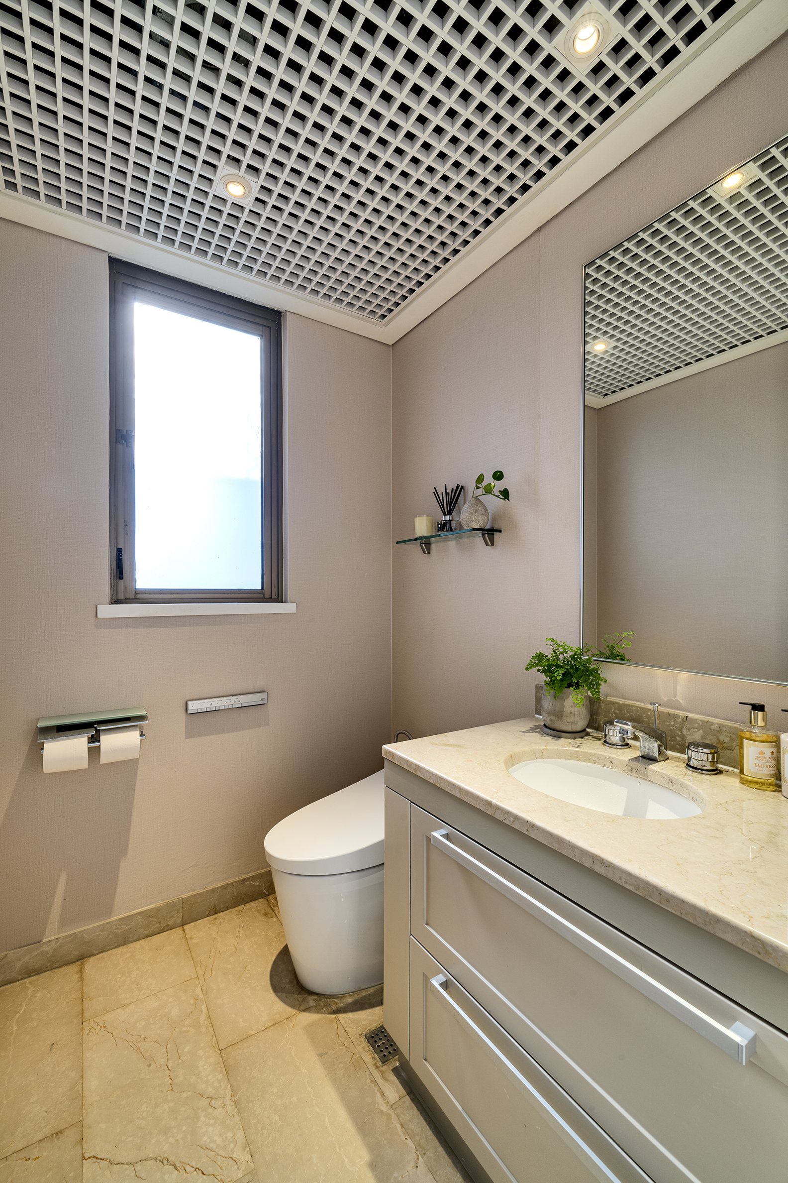 Modern bathroom featuring a white toilet, stone countertop vanity with sink, mirror, and a distinctive grid ceiling design.