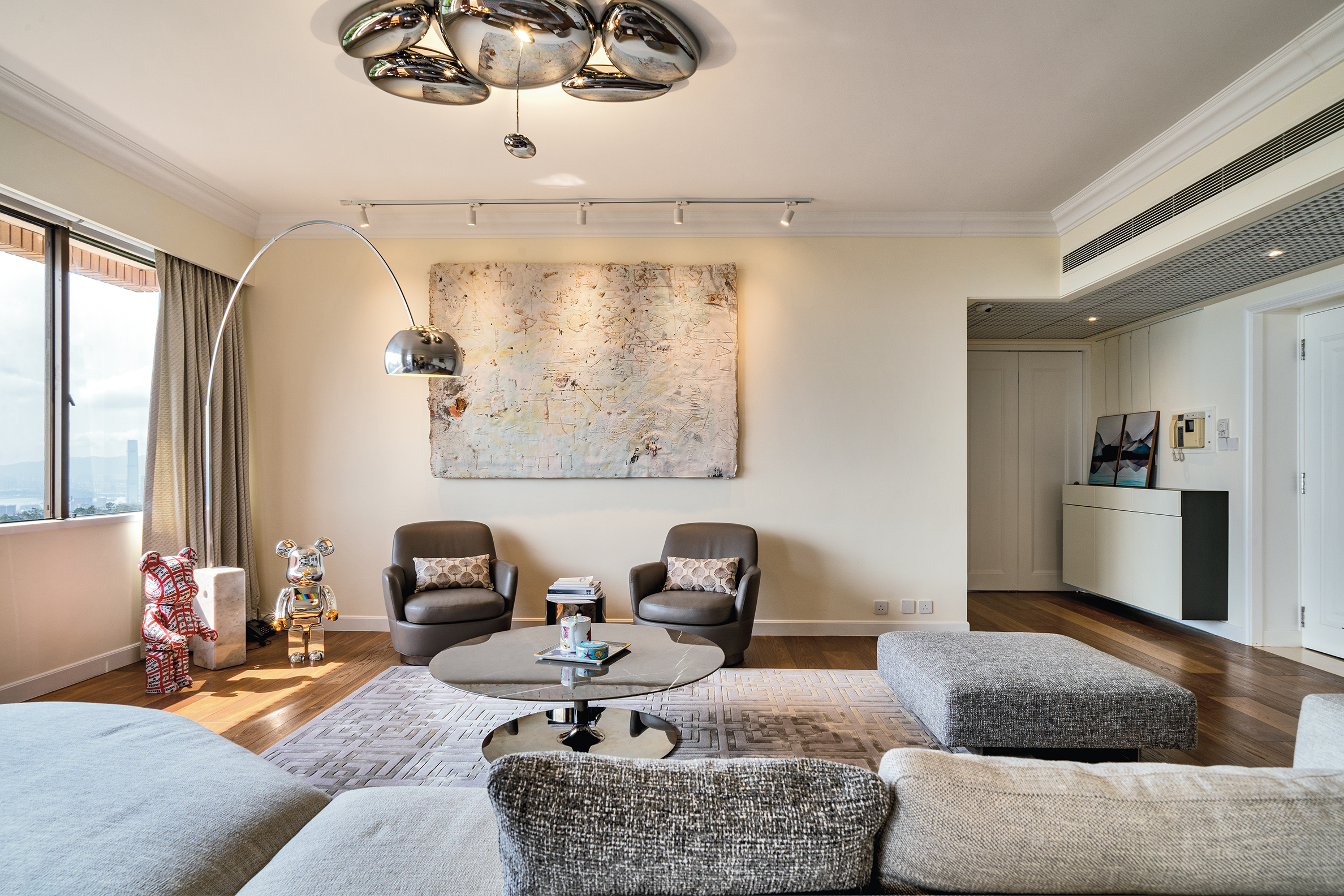 A living room with grey fabric sofas, a round marble coffee table, an arched floor lamp, and a large abstract painting.