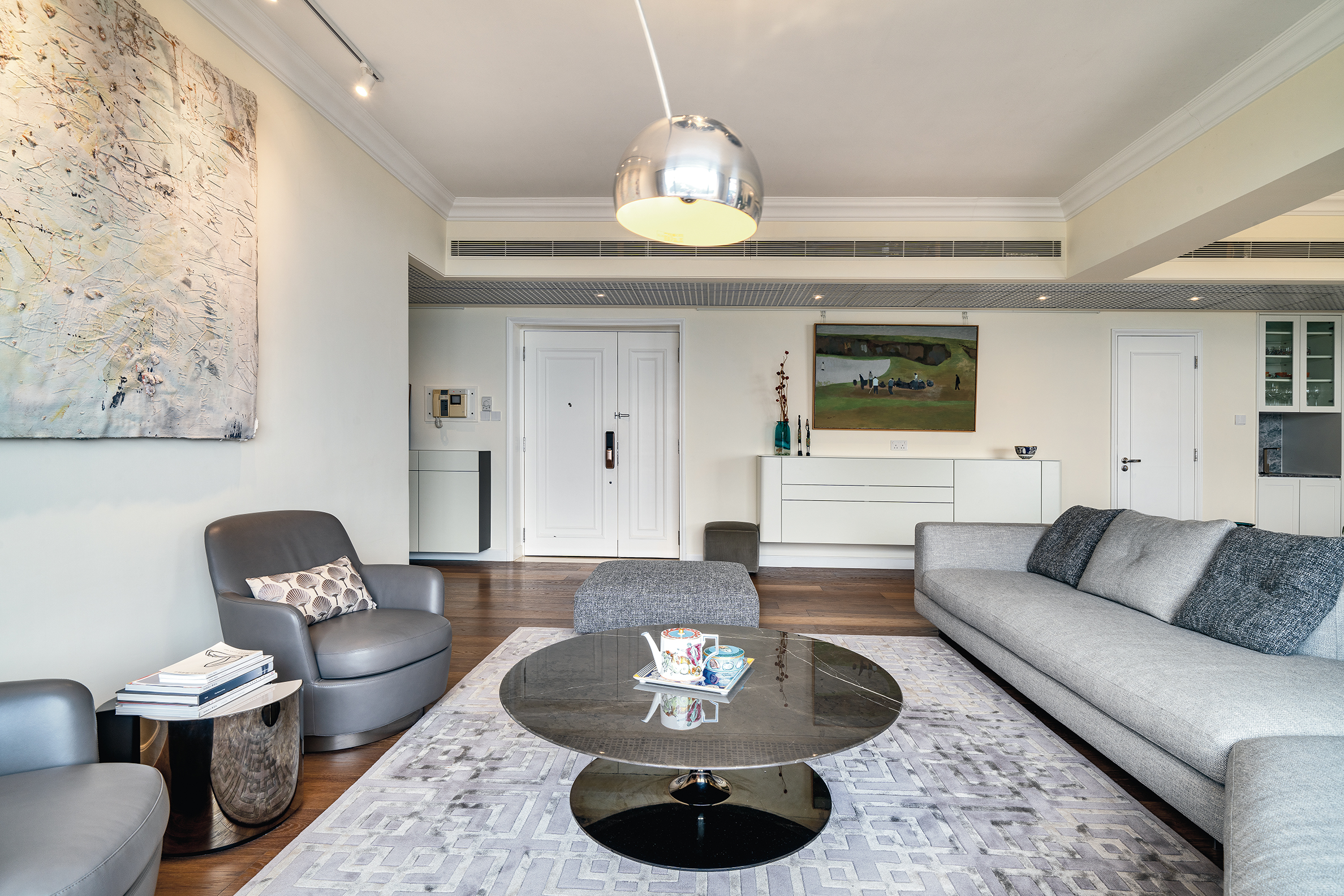 Spacious living room featuring a grey sofa, round black marble coffee table, silver dome pendant light, and large abstract painting.