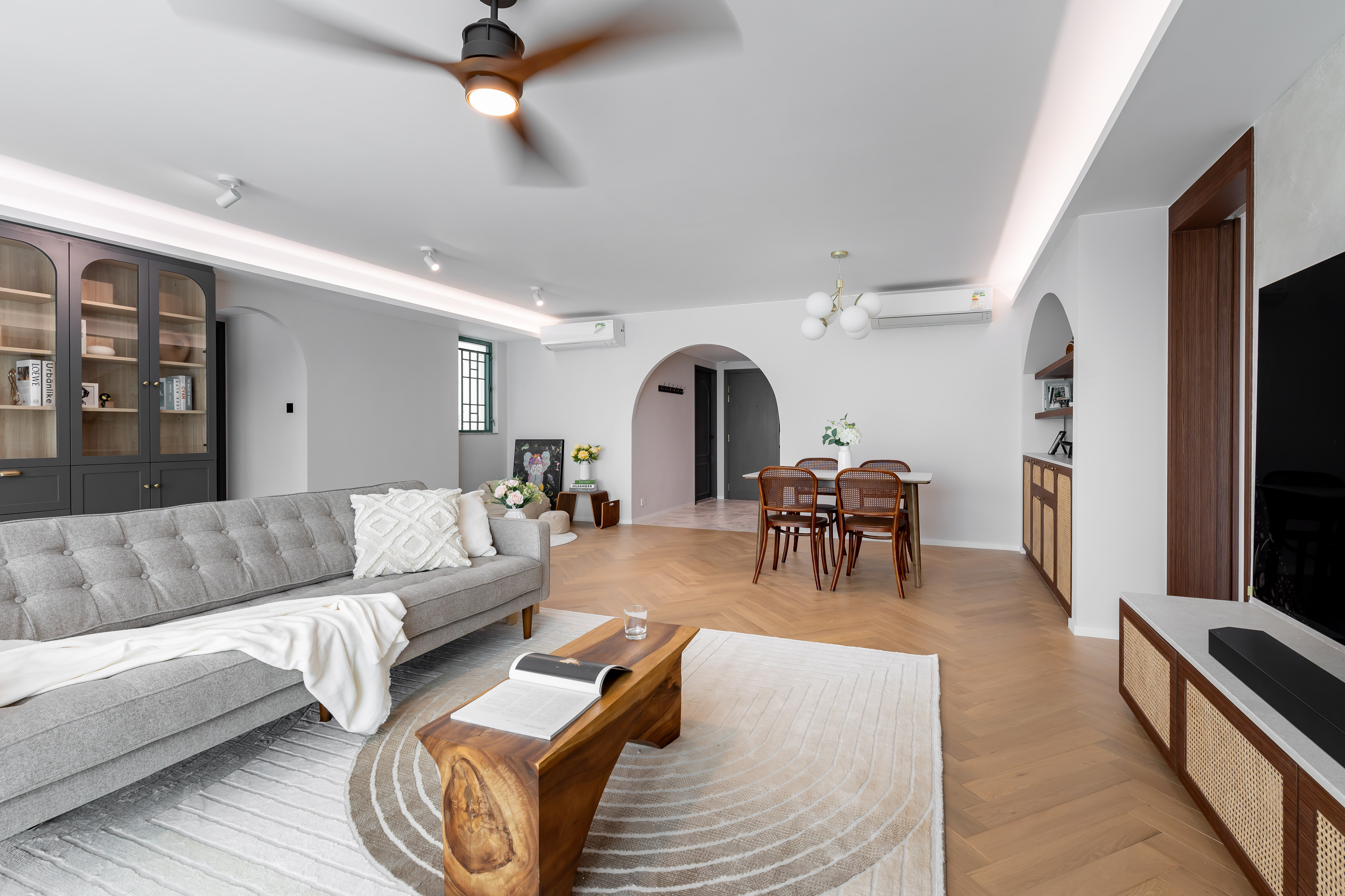 A spacious living and dining room featuring a grey sofa, wooden coffee table, dining set, and arched doorways.