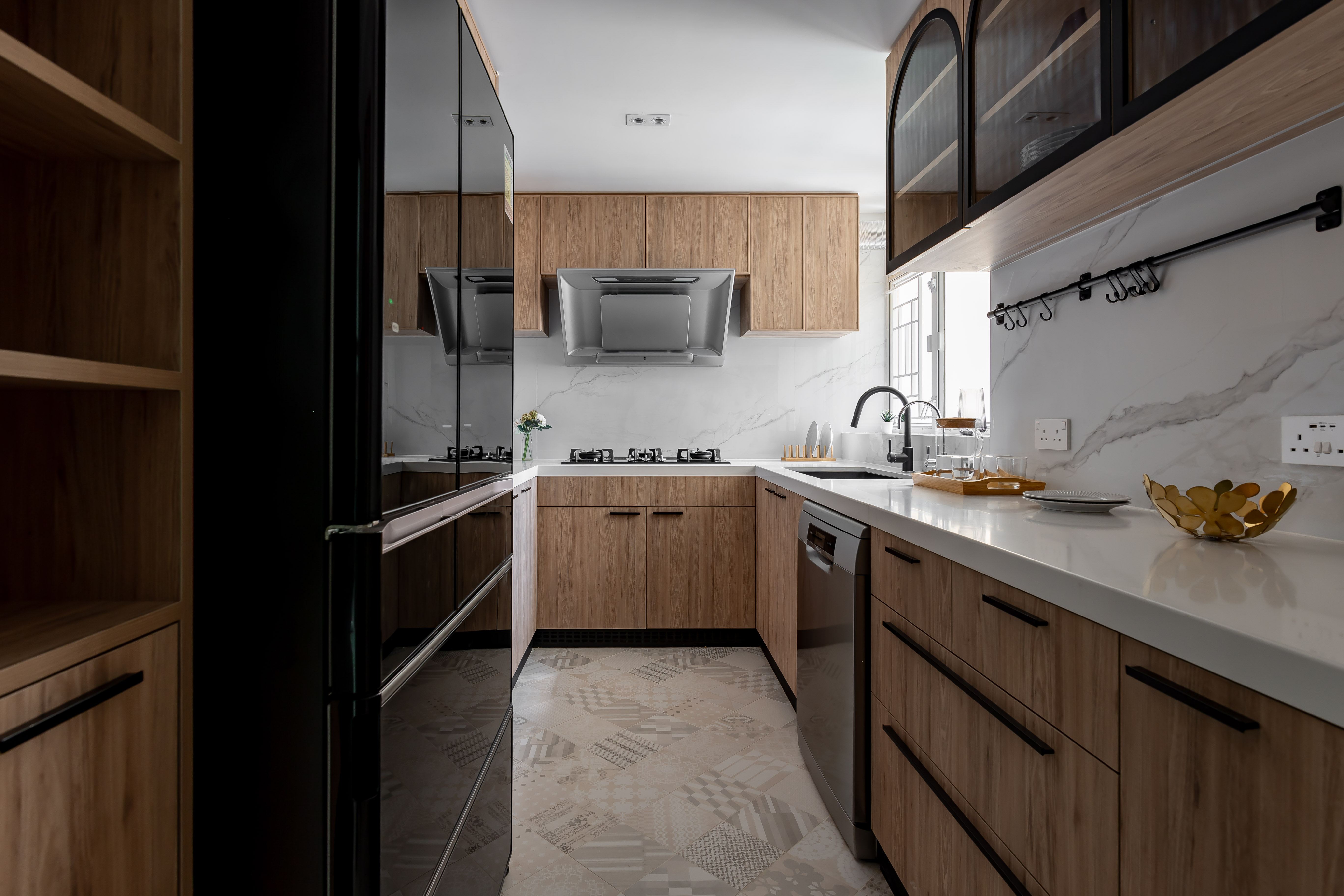 A modern kitchen featuring wooden cabinets, white marble countertops, a stainless steel range hood, and patterned floor tiles.