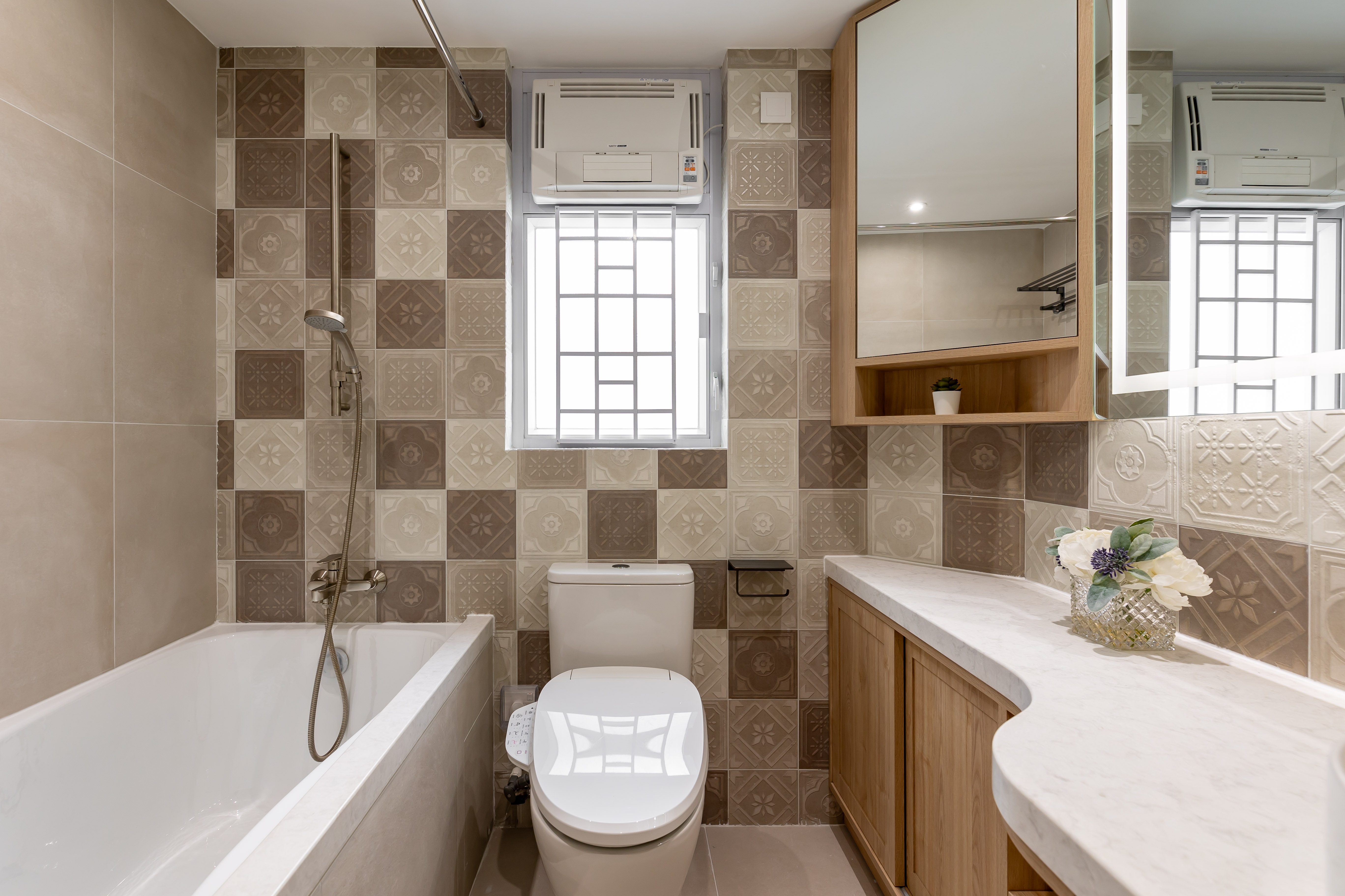 Bathroom with patterned wall tiles, a white bathtub, a toilet, and a wooden vanity with a mirror cabinet.