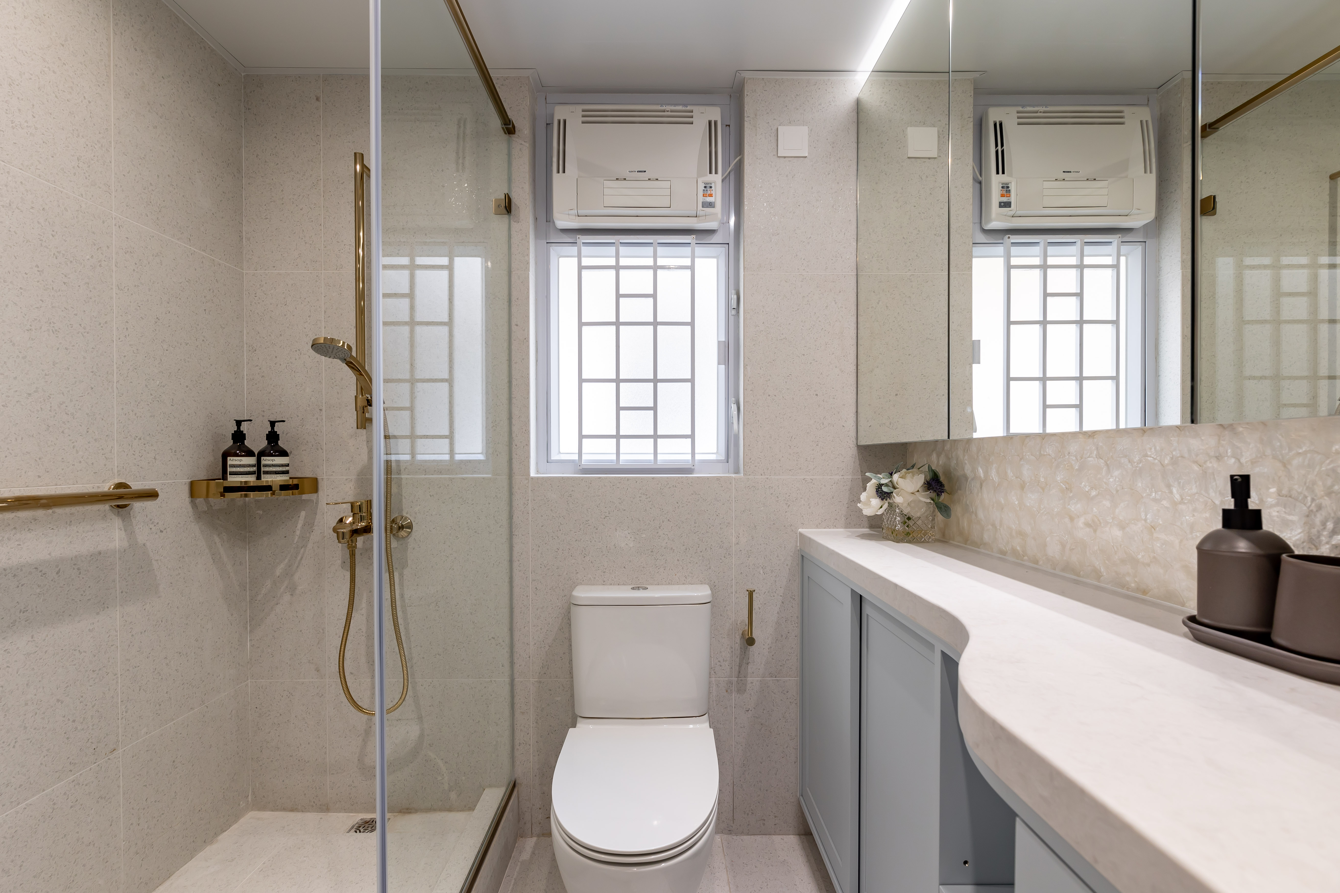 A modern bathroom featuring a glass shower enclosure with gold fixtures, a white toilet, and a vanity with light blue cabinets.