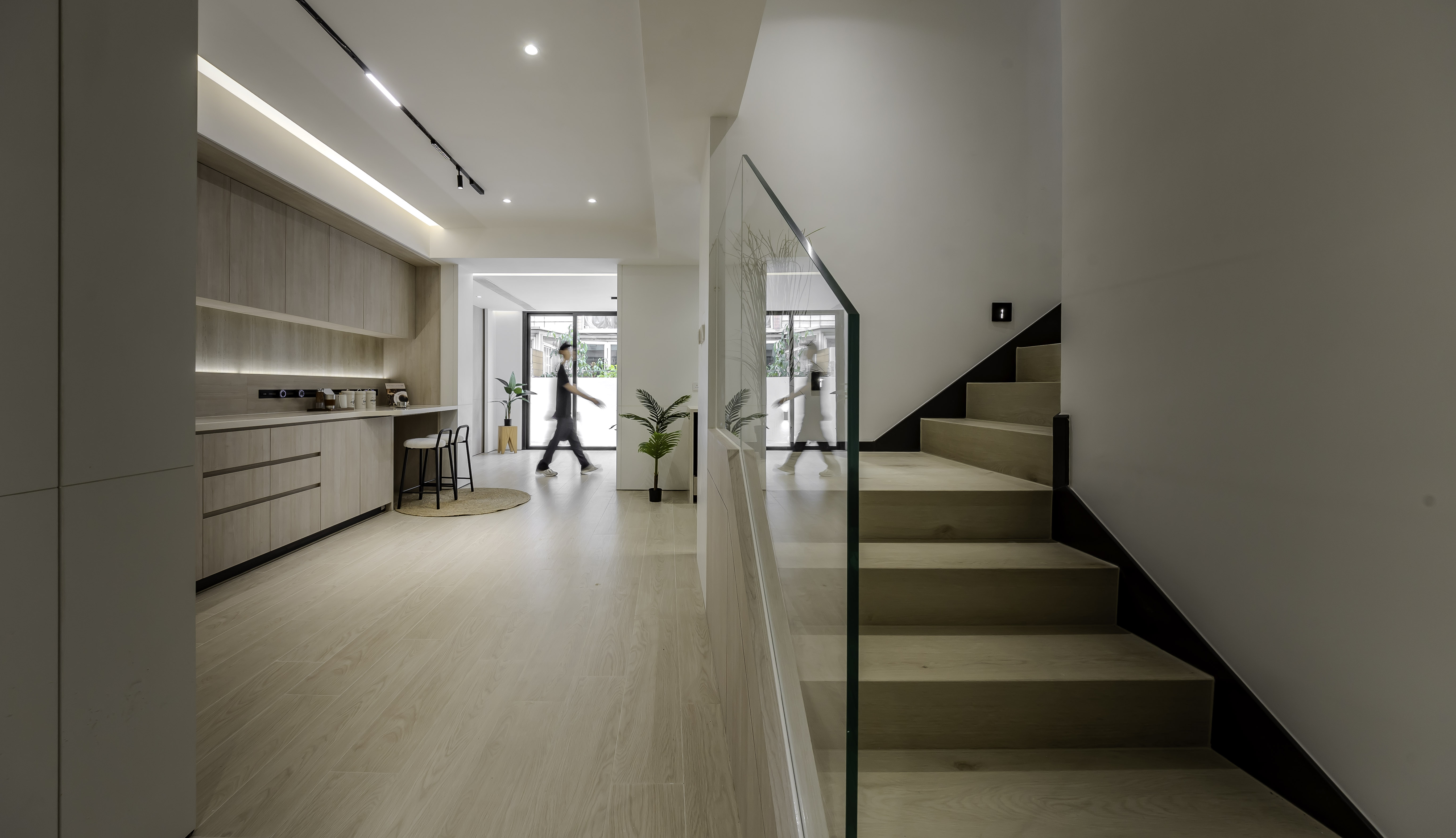 Modern interior featuring light wood kitchen cabinets with a bar counter, and a wooden staircase with a glass railing.