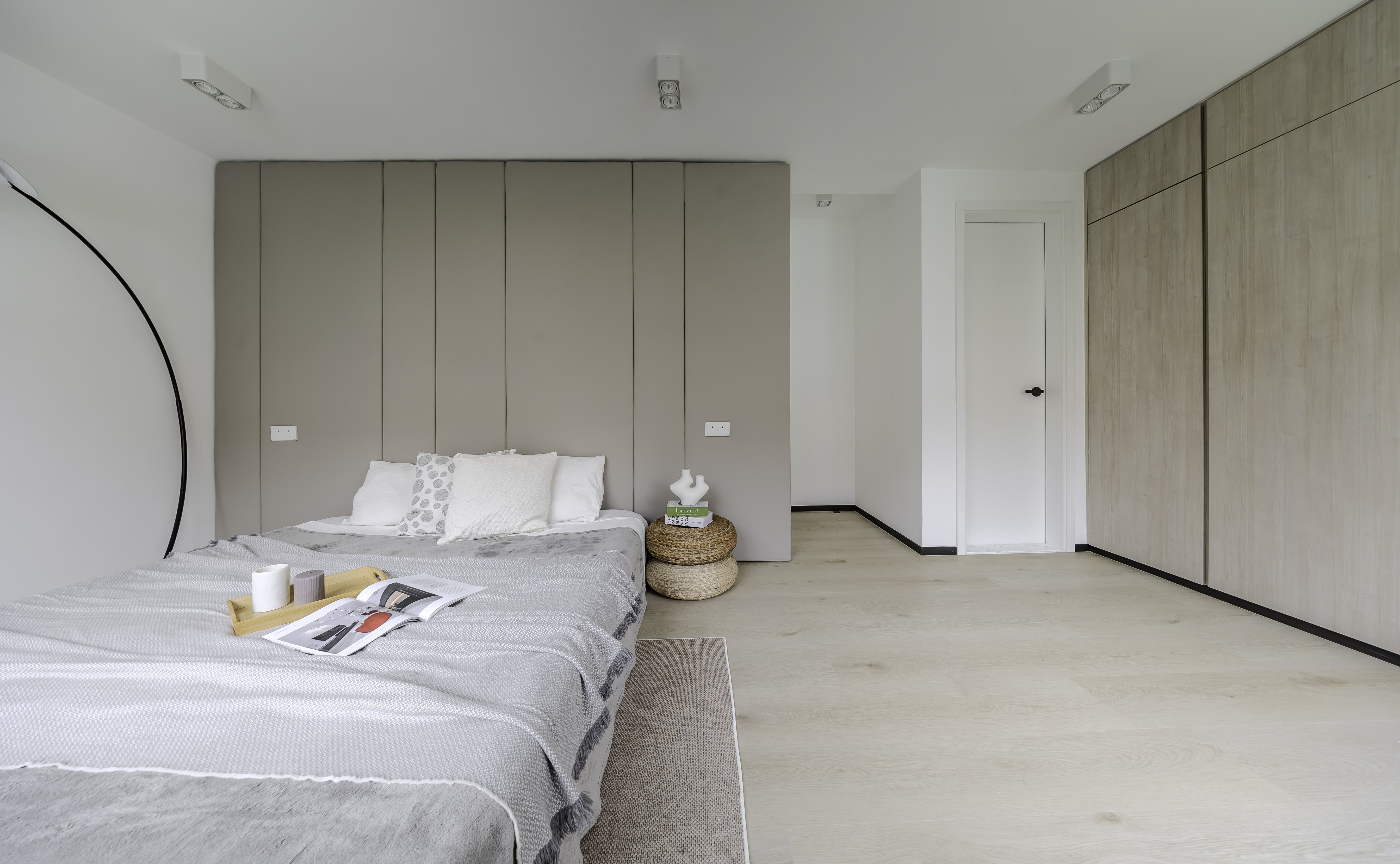 A modern bedroom featuring a bed with a beige paneled headboard, light wood flooring, and a large wooden wardrobe.