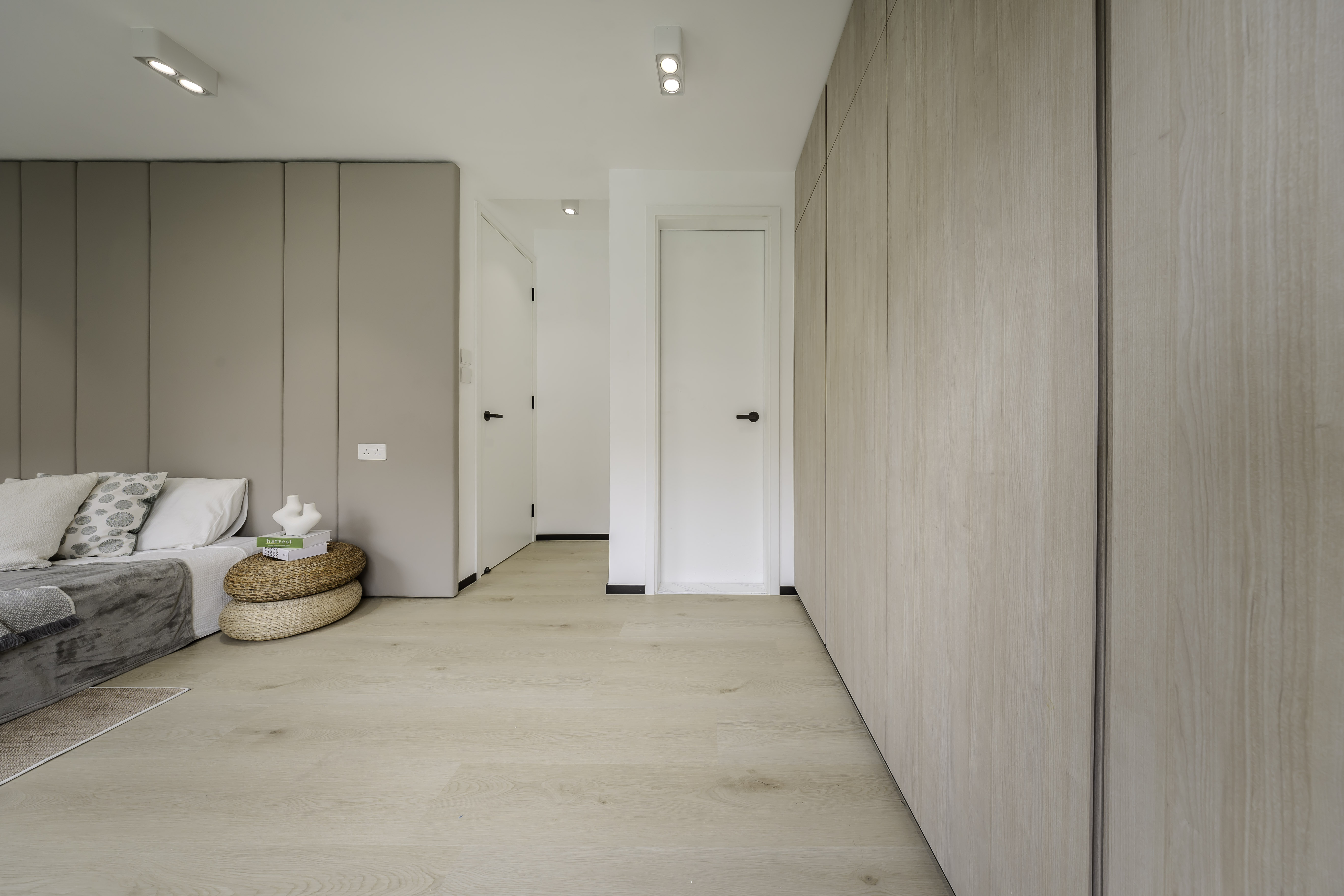 A modern bedroom featuring a bed with a beige padded headboard, light wood flooring, and extensive light wood built-in wardrobes.